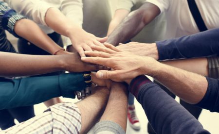 diverse group of people putting their hands in the middle of a circle