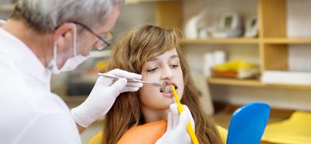 Teenage girl with the braces on her teeth is having a treatment at dentist